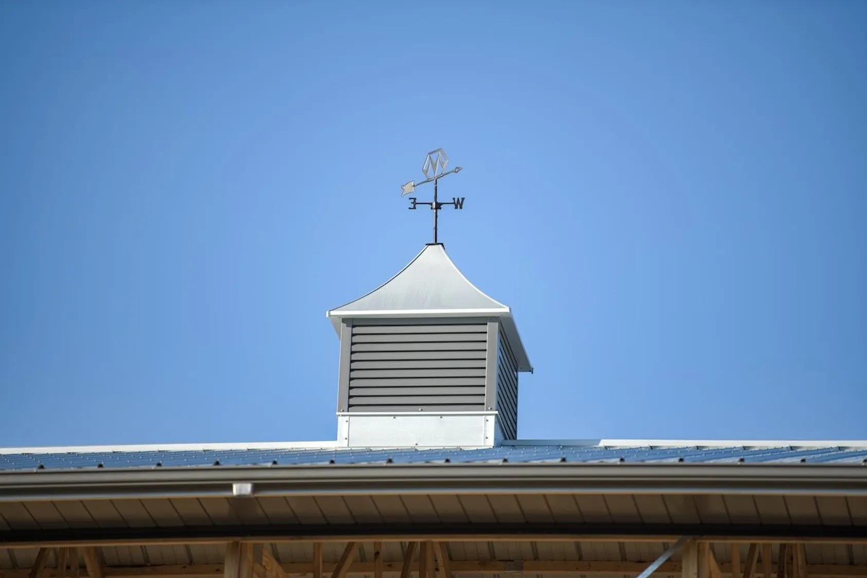 White cupola with louvered vents and deer weathervane on blue metal roof against clear sky