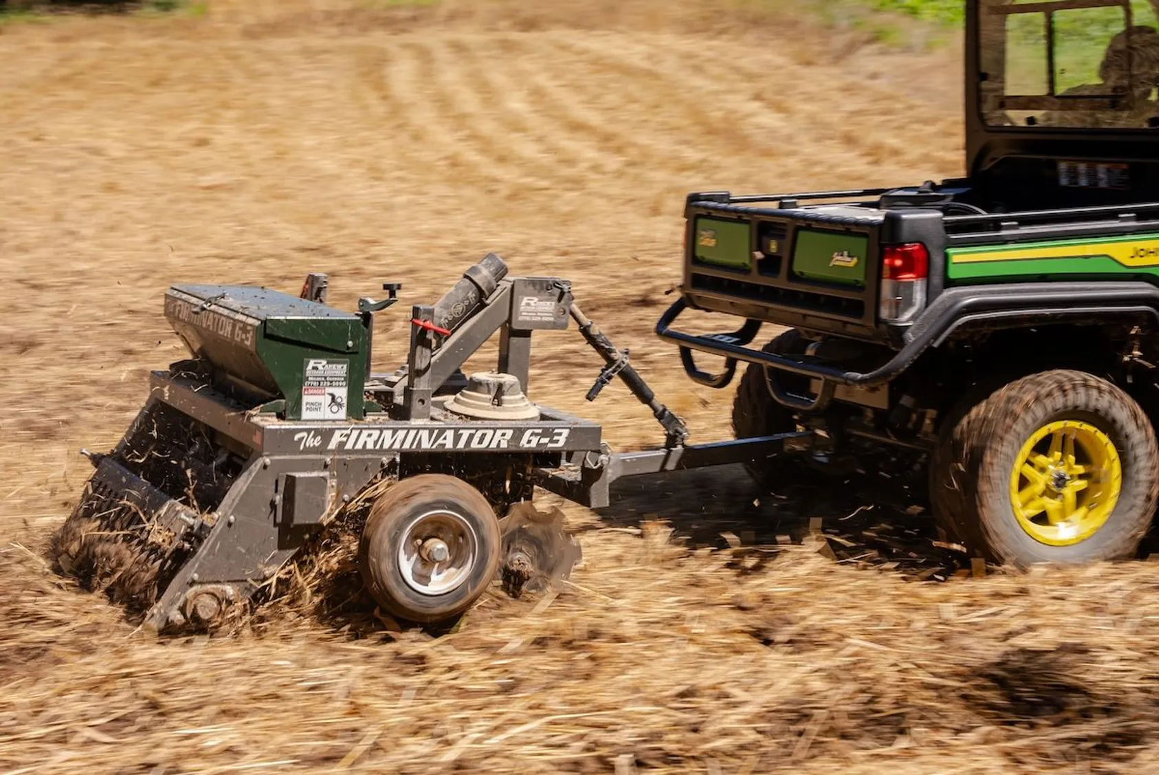 John Deere utility vehicle towing a Firminator G-3 seeding implement across tilled soil
